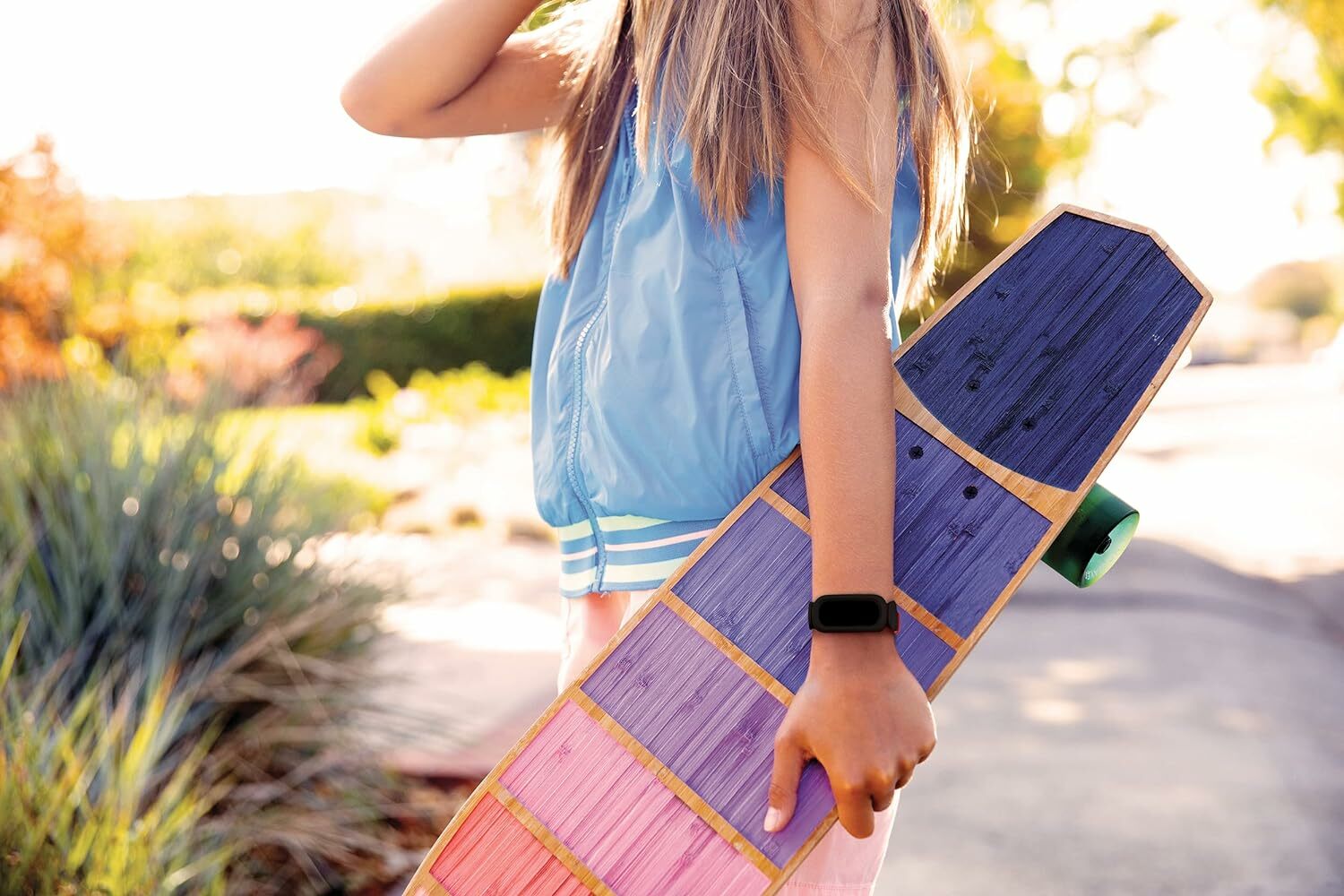 A young girl hold a longboard and wears a Fitbit
