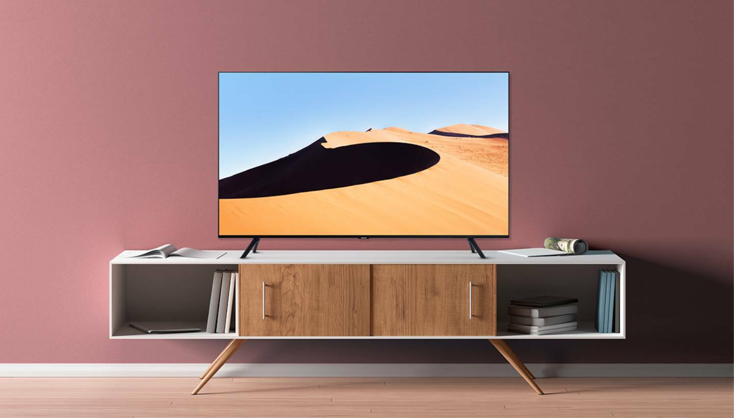 Samsung 4K TV with sand dune screensaver sitting on TV stand with pink wall in background
