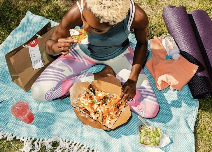a person sits on a picnic blanket with food delivery from doordash
