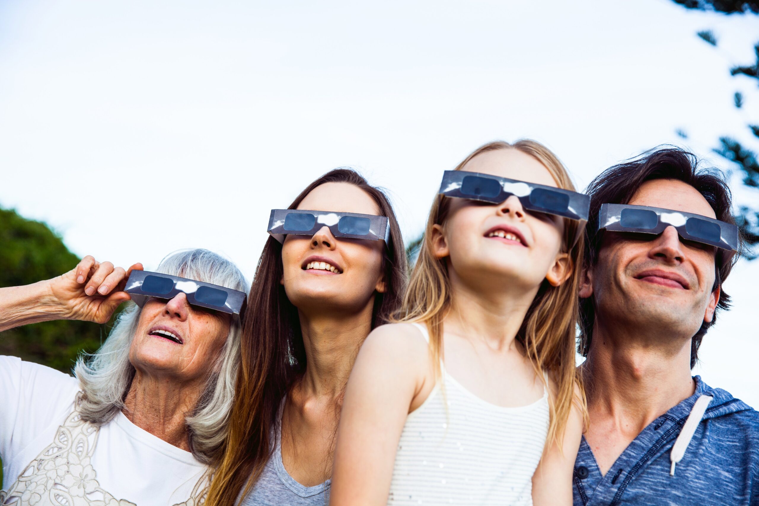 four people wear solar eclipse glasses while looking into the sky