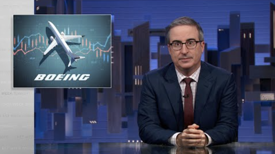 A man sits behind a talk show desk with an image of a Boeing airplane in the top left.