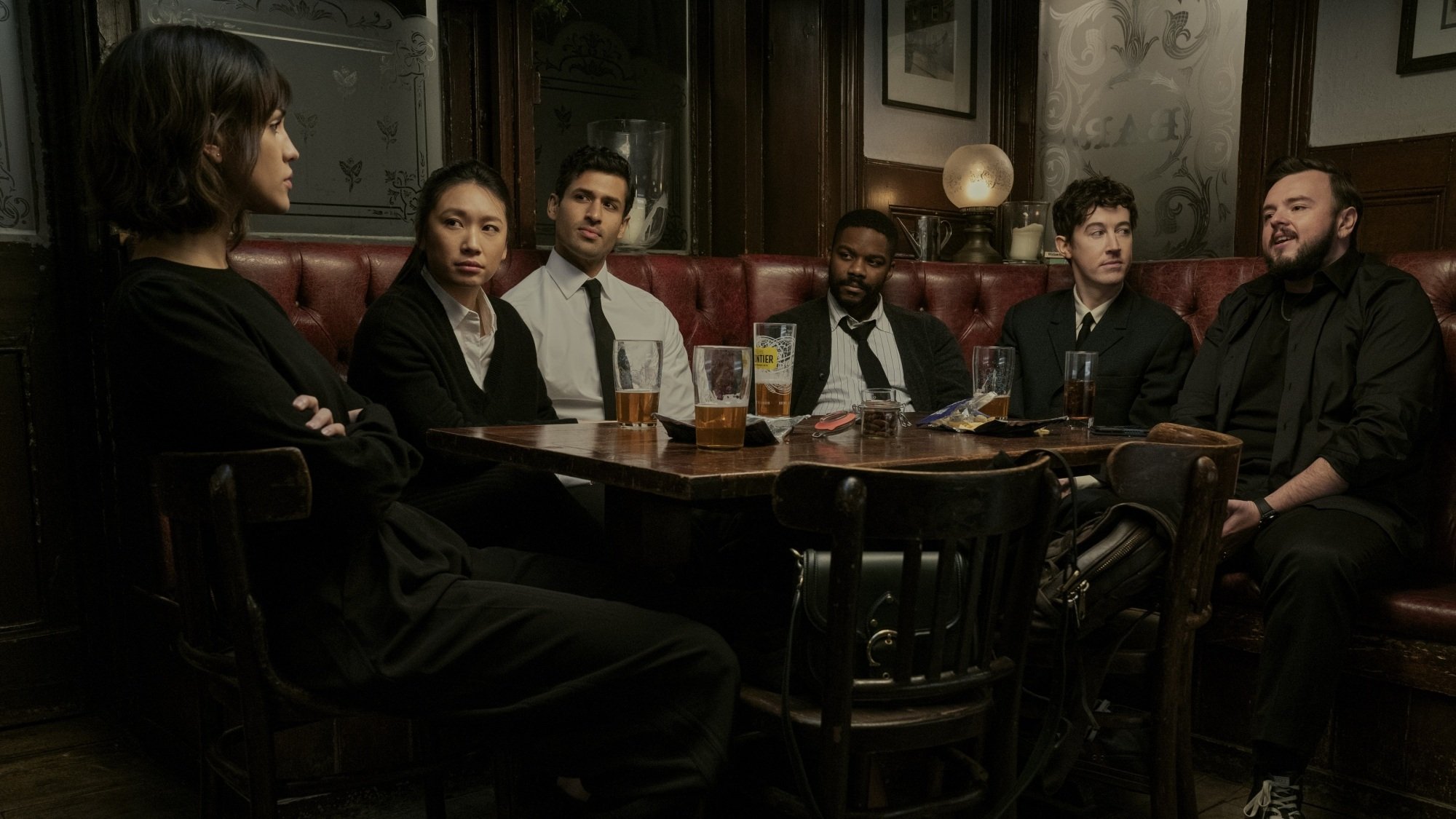 A group of friends dressed in black sit around a table at a pub.