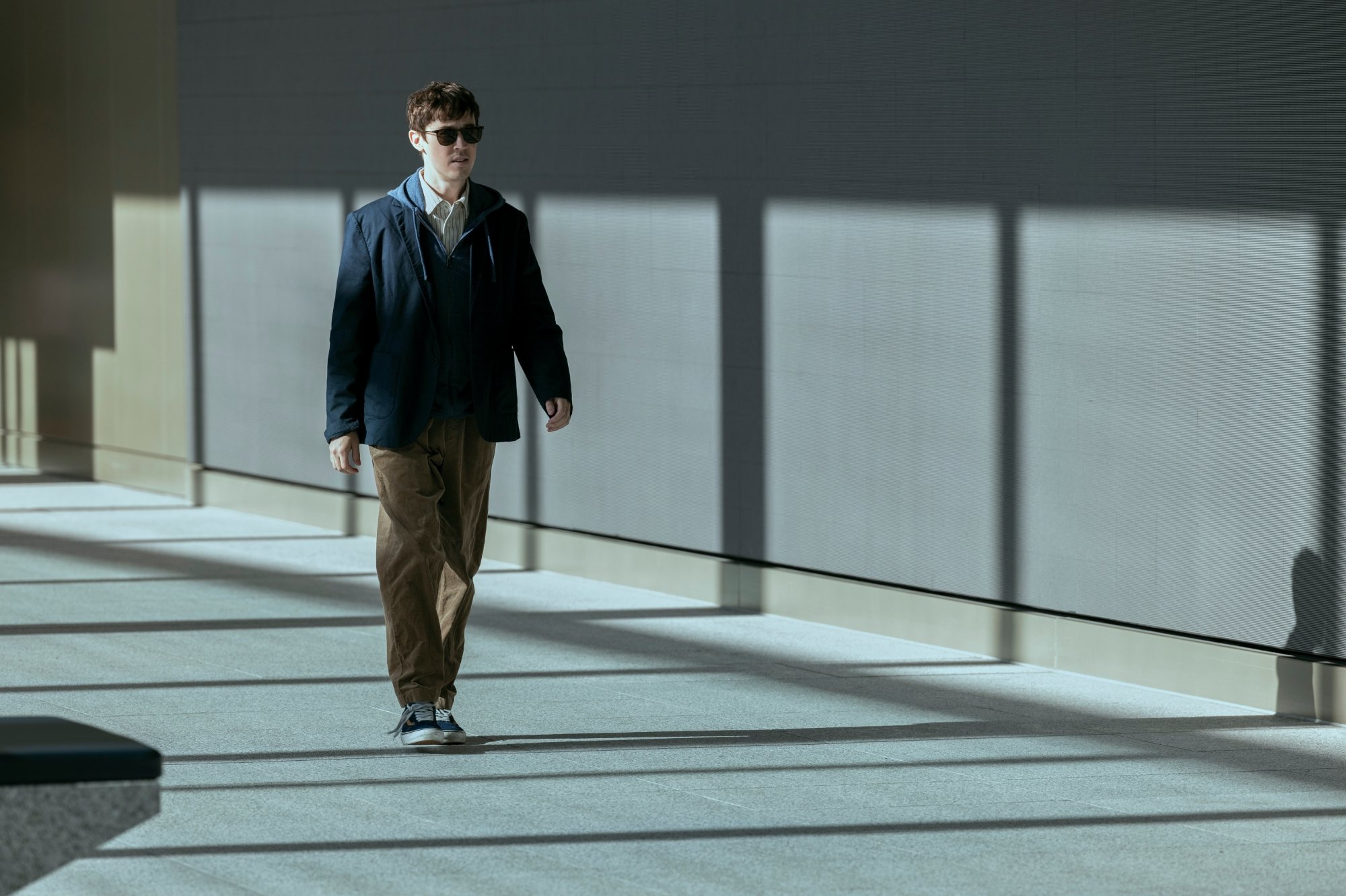 A man wearing sunglasses walks through a sparse building lobby.