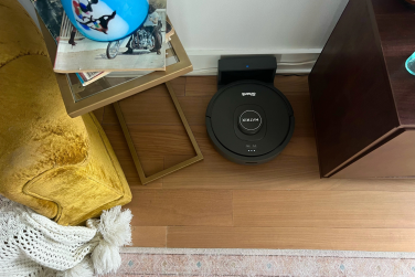 Shark Matrix robot vacuum and dock sitting on hardwood floor between TV stand and end table with yellow armchair in peripheral