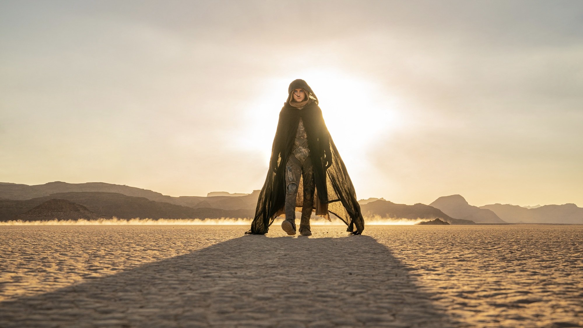 Paul Atreides walks through the desert in a cloak and stillsuit.