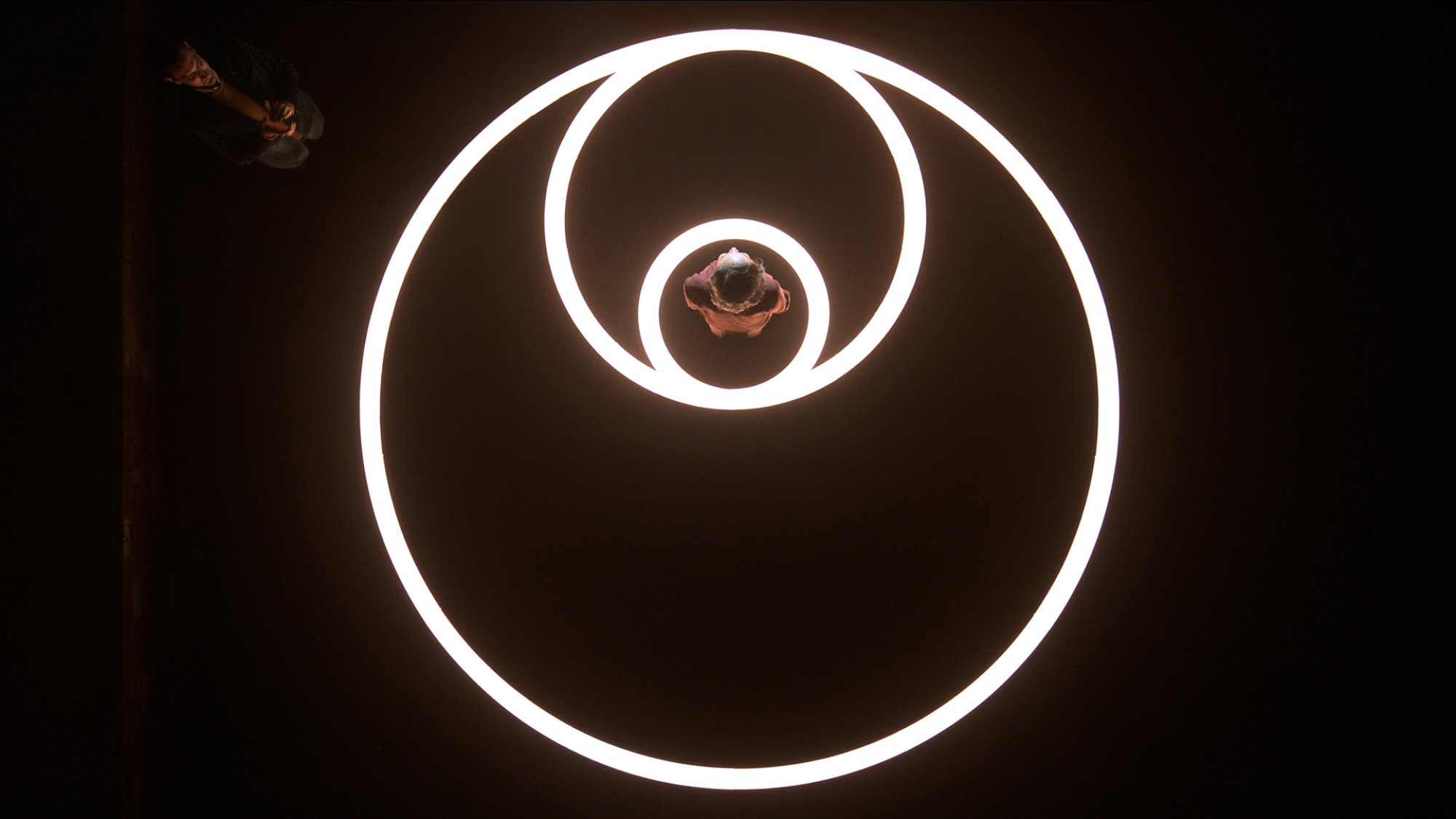 A woman stands in the middle of three glowing circles, seen from overhead.