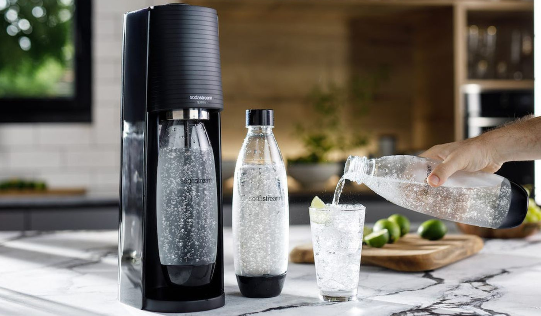 Person pouring sparkling water into glass next to SodaStream sparkling water maker on countertop