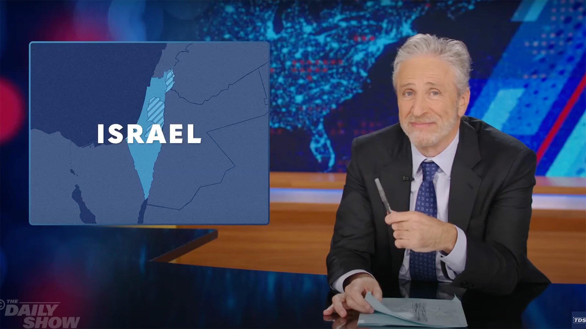 A man sits at a talk show desk while Israel is shown on a map in the top-left corner.
