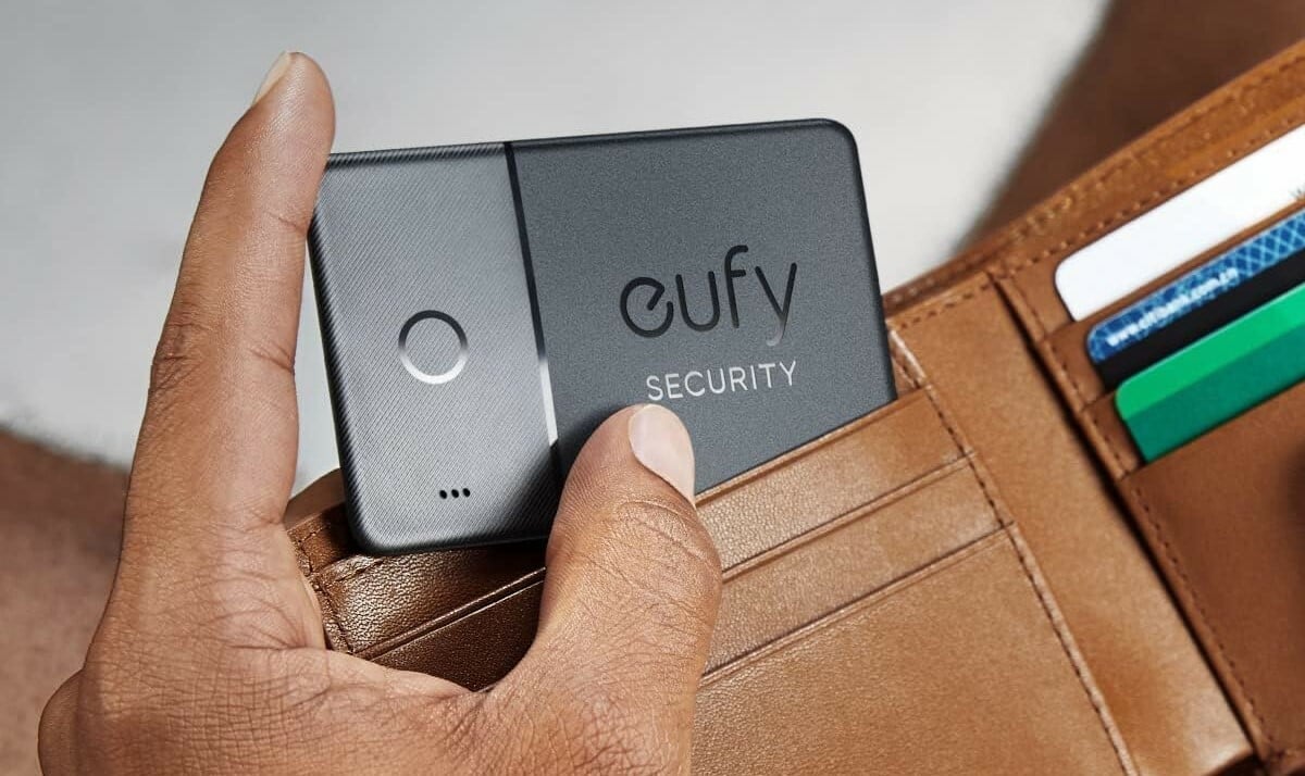 a person's left hand puts a eufy by anker smarttrack card into a brown leather wallet