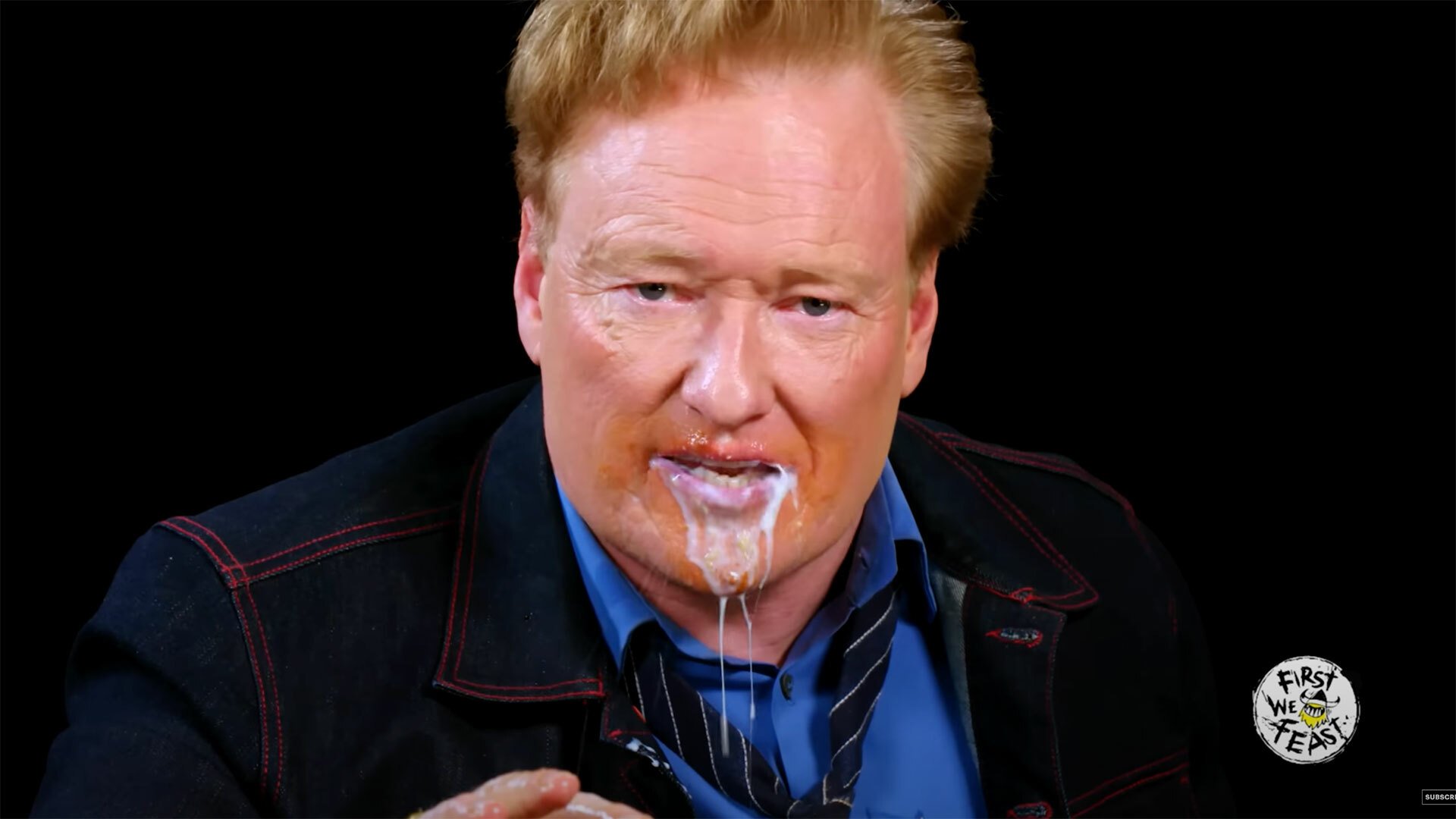 A man in a dark room dribbles milk from his mouth while staring at the camera.