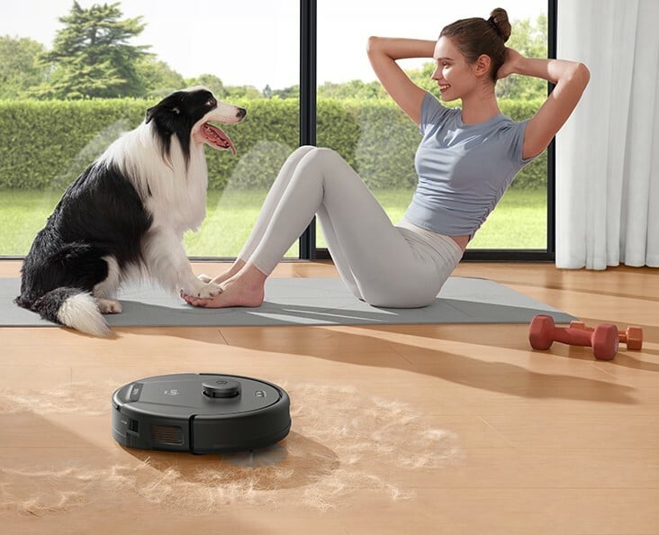 A woman does pilates with her dog while the eufy robot vacuum cleans pet hair