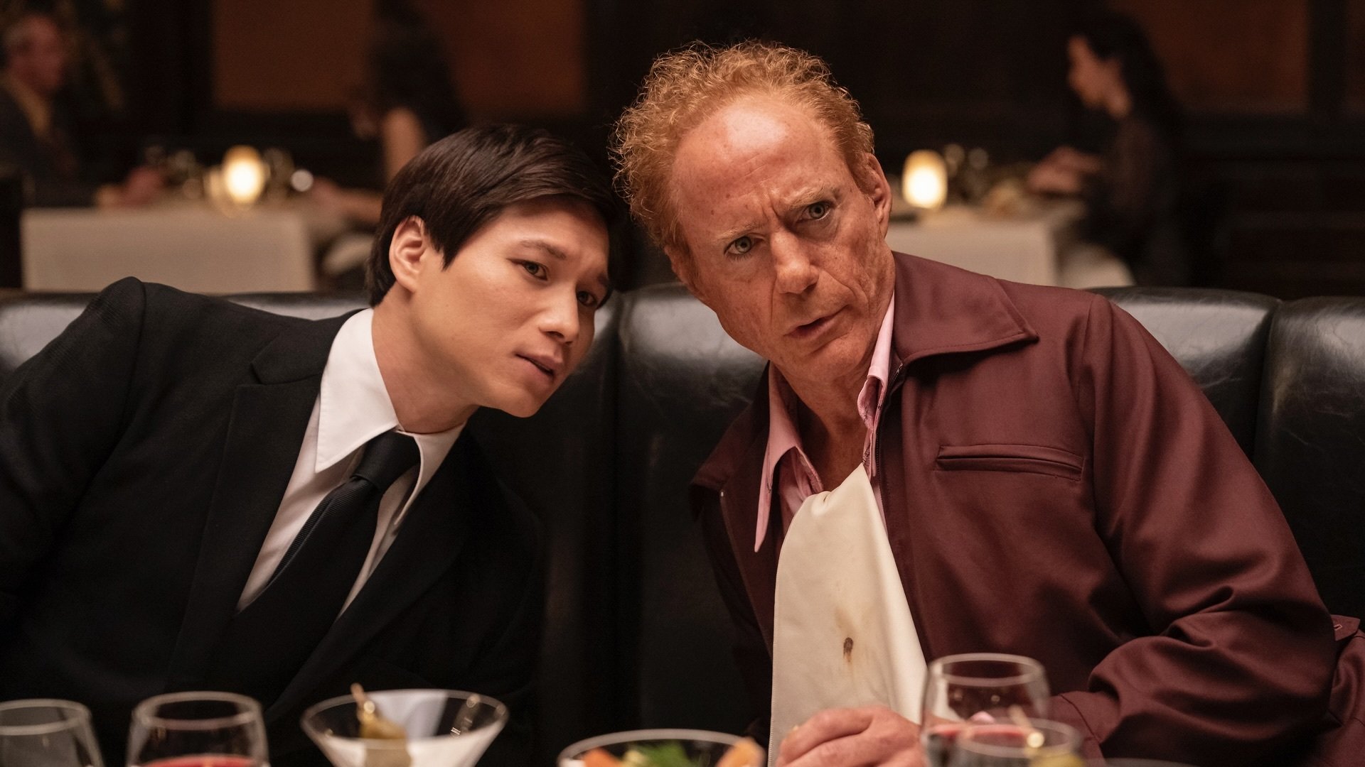 Two men lean together to discuss something while eating at a steakhouse.
