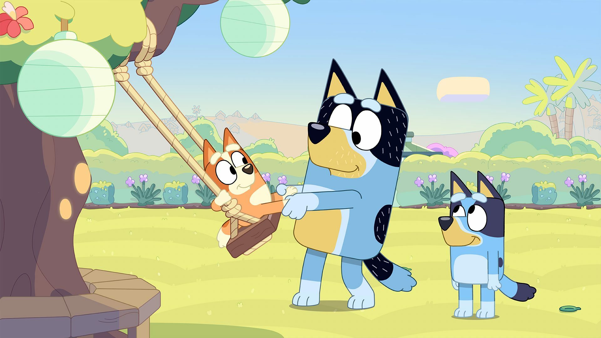 Bandit pulling Bingo on a swing while Bluey watches.