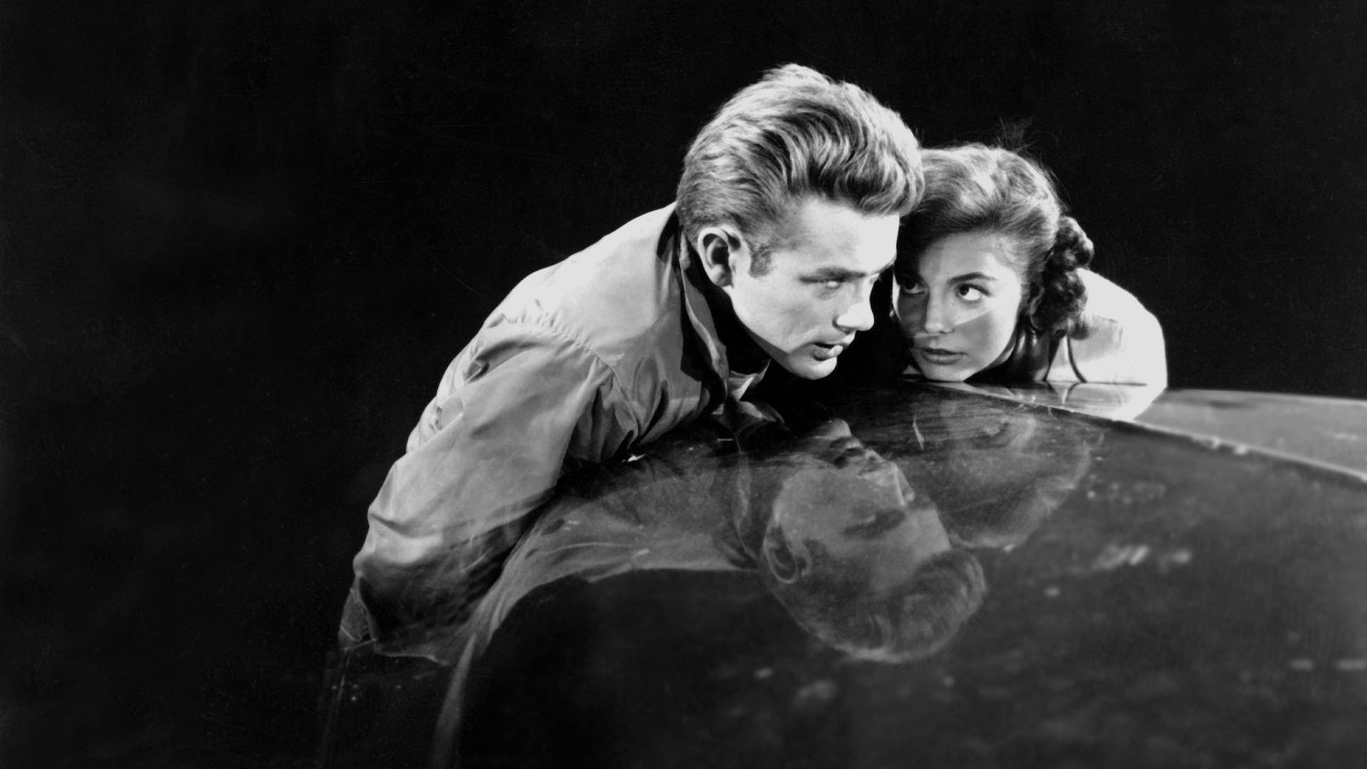 James Dean and Natalie Wood huddle together on the bonnet of a car in the film 