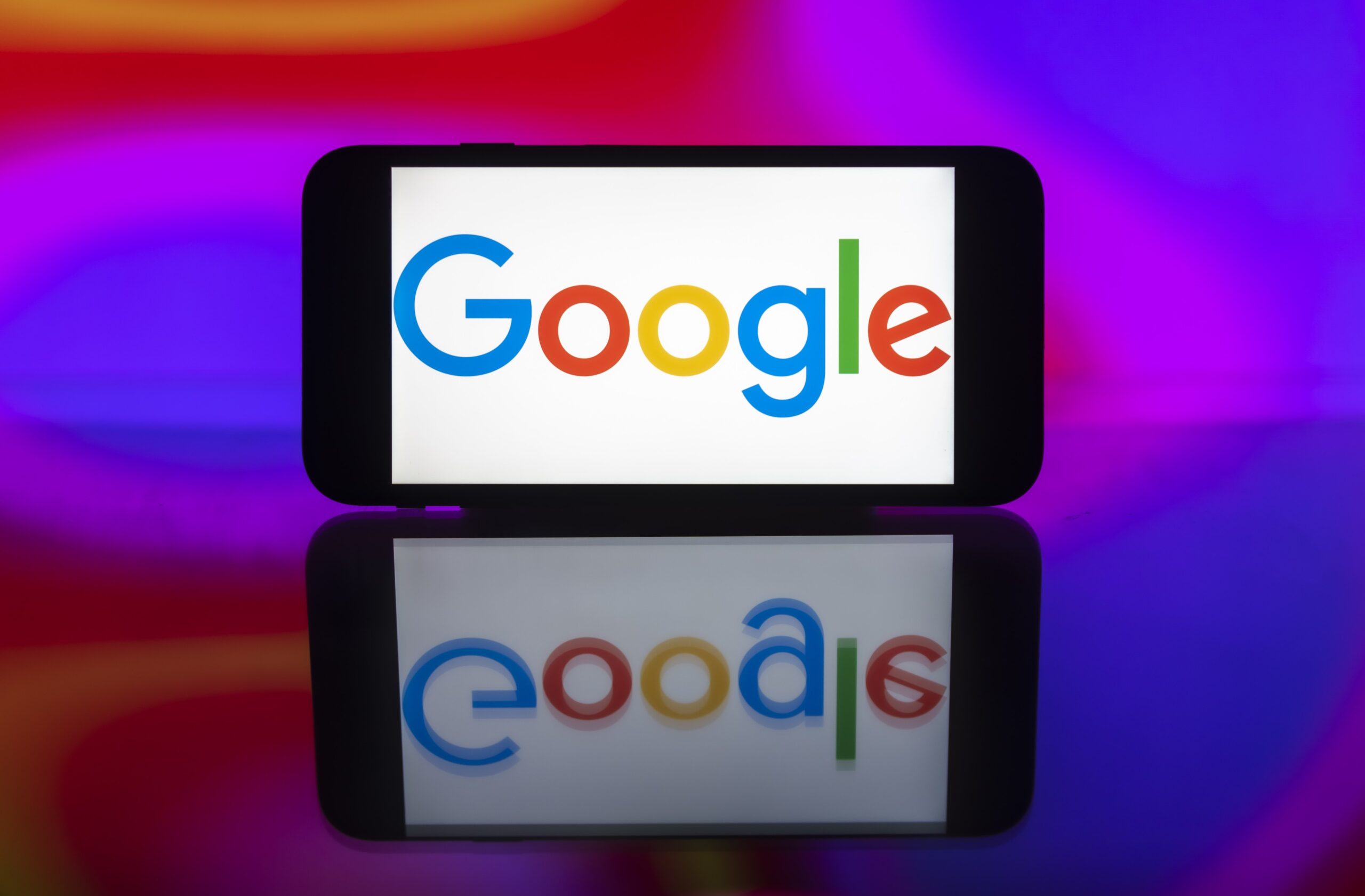 A phone showing the Google logo on a colorful, reflective backdrop.