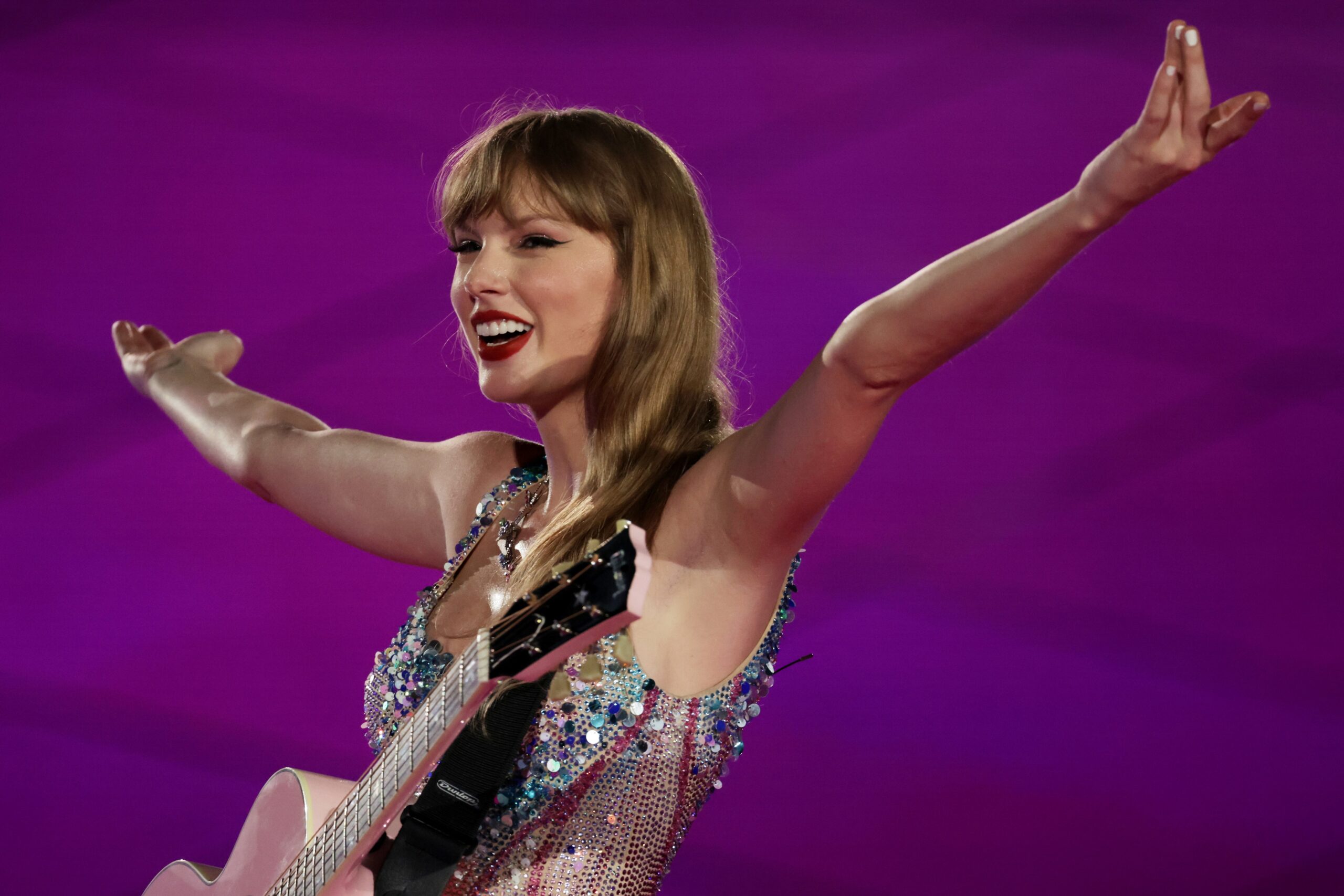Taylor Swift smiling and raising her arms while performing at The Eras Tour.