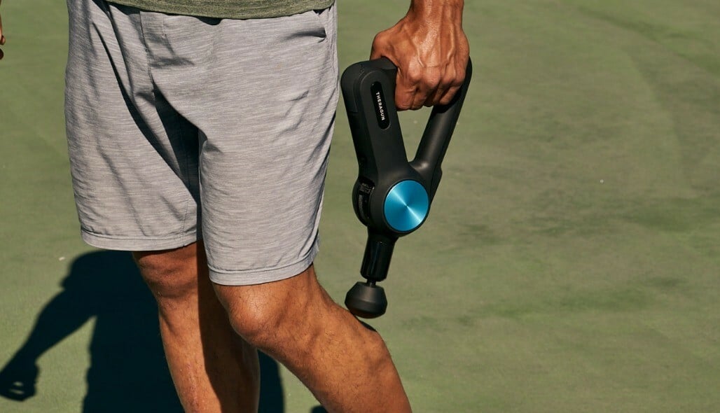 a person standing on a tennis court uses the theragun pro on his left calf muscle