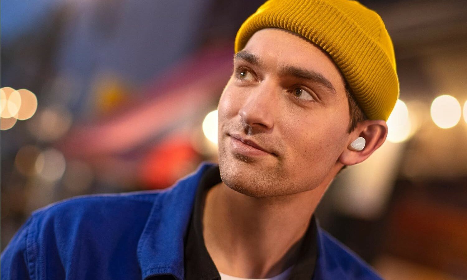 a person wearing a yellow beanie smiles while looking off to the left while wearing the jabra elite 5 earbuds