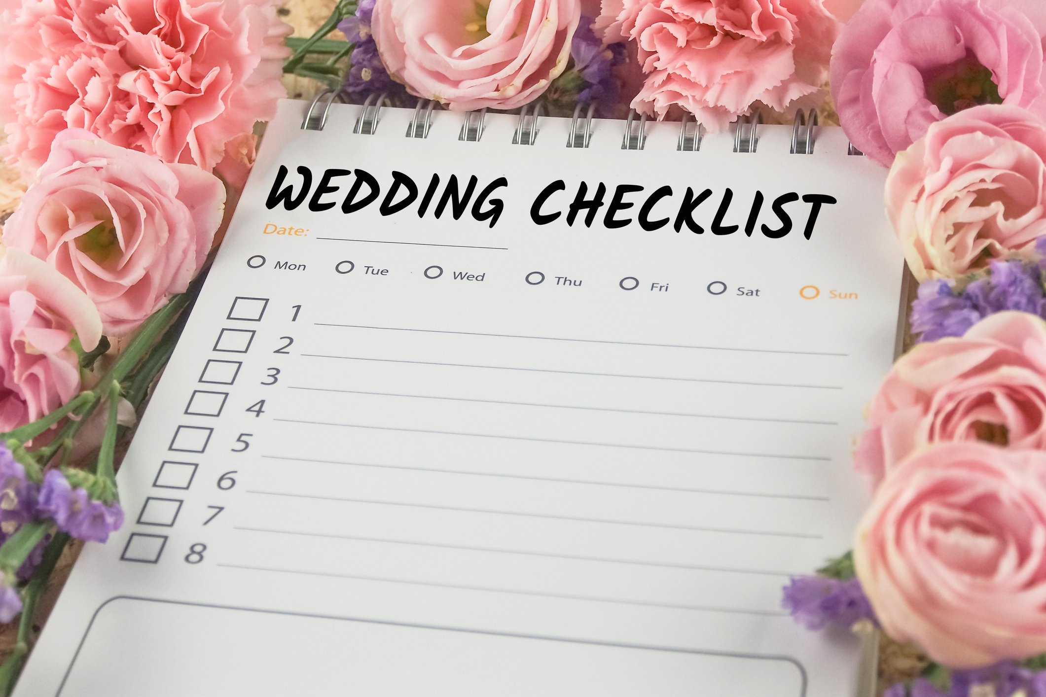 a blank wedding checklist on a bed of pink roses