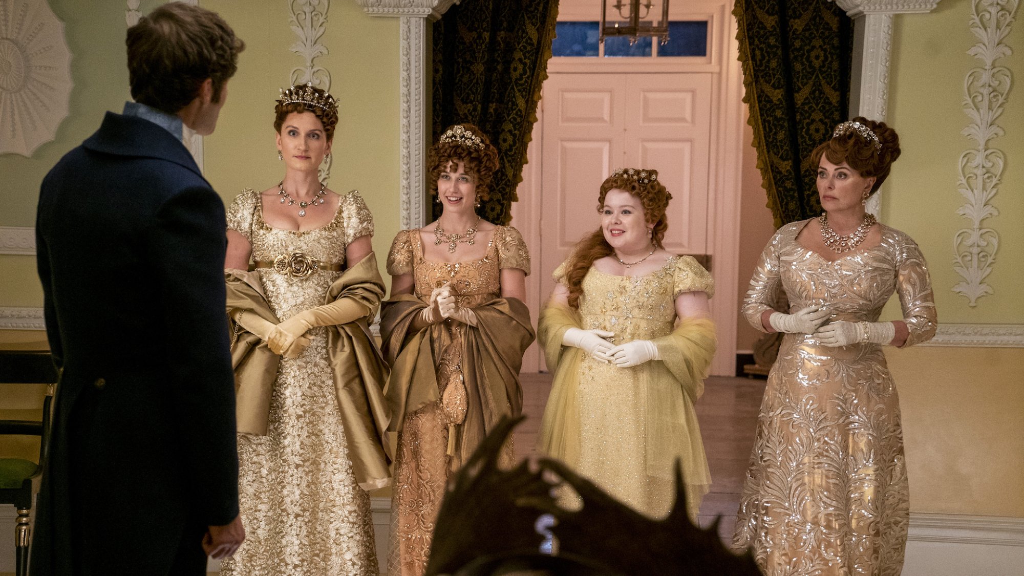 Rupert Young as Lord Jack Featherington, Bessie Carter as Prudence Featherington, Harriet Cains as Philipa Featherington, Nicola Coughlan as Penelope Featherington, Polly Walker as Lady Portia Featherington, standing in a row in the show "Bridgerton"