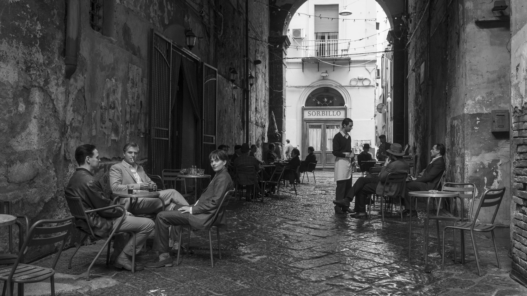 Three people drink coffee in an Italian laneway.