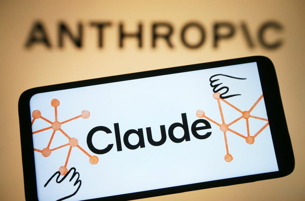 The Claude app logo on a smartphone in front of a projection of the Anthropic logo