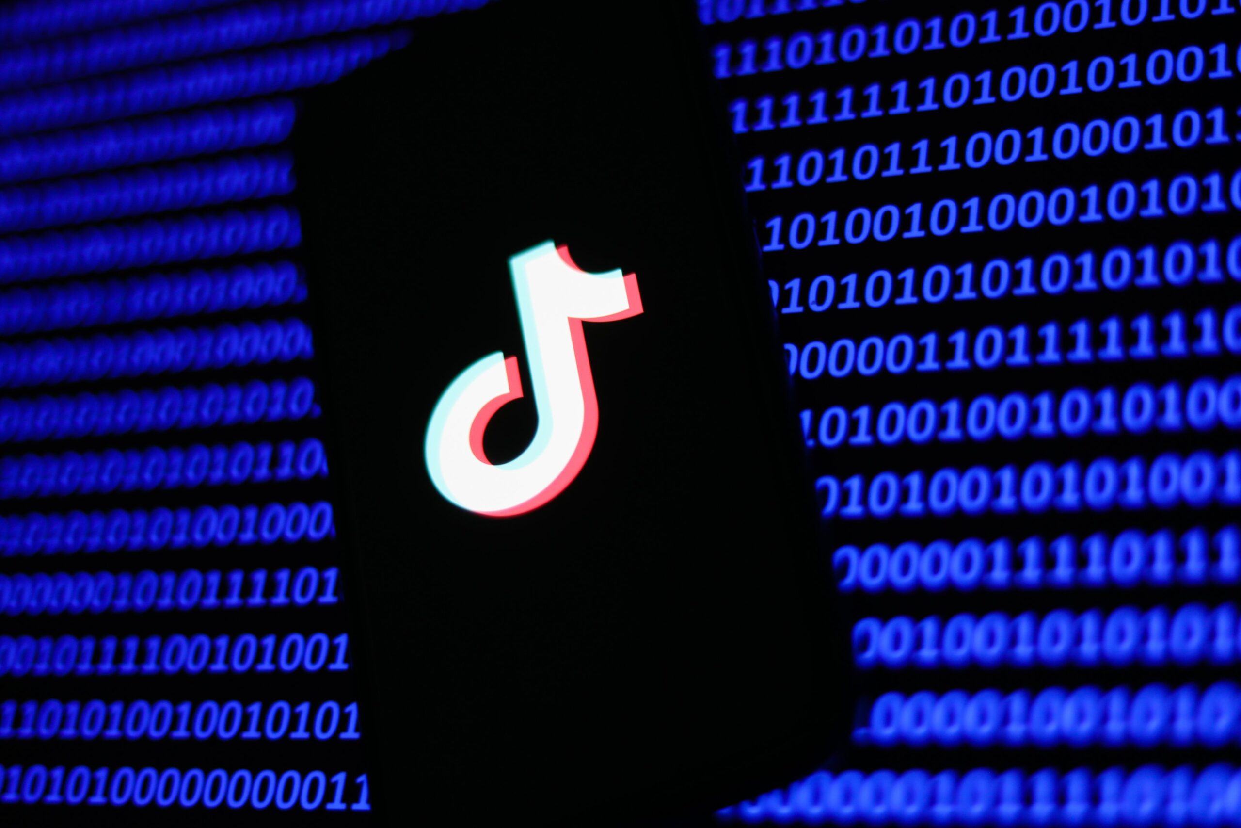 A phone showing the TikTok label in front of lines of binary code.