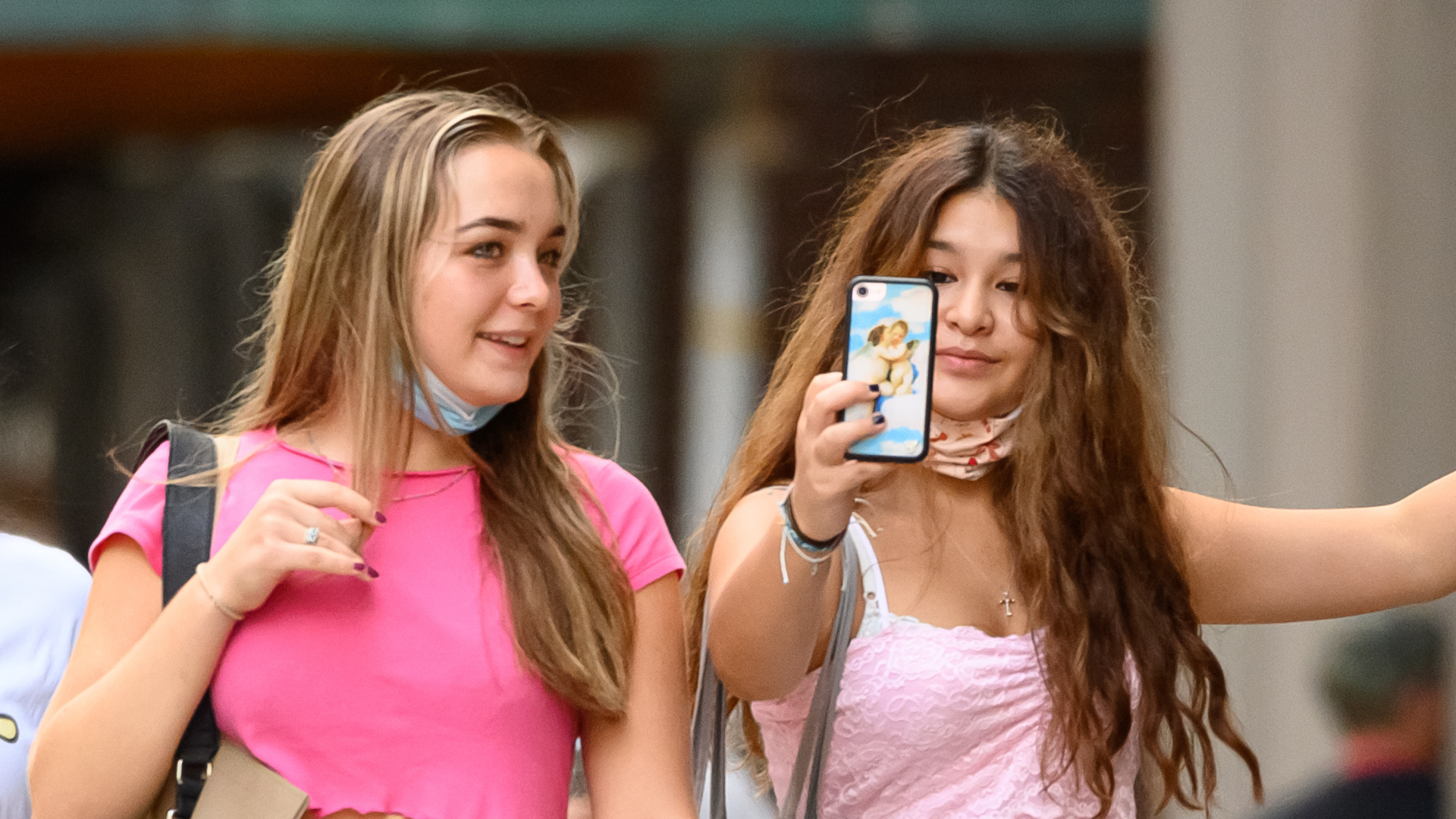 Two teen girls in pink tops. One holds a mobile phone in front of her as if taking a selfie.
