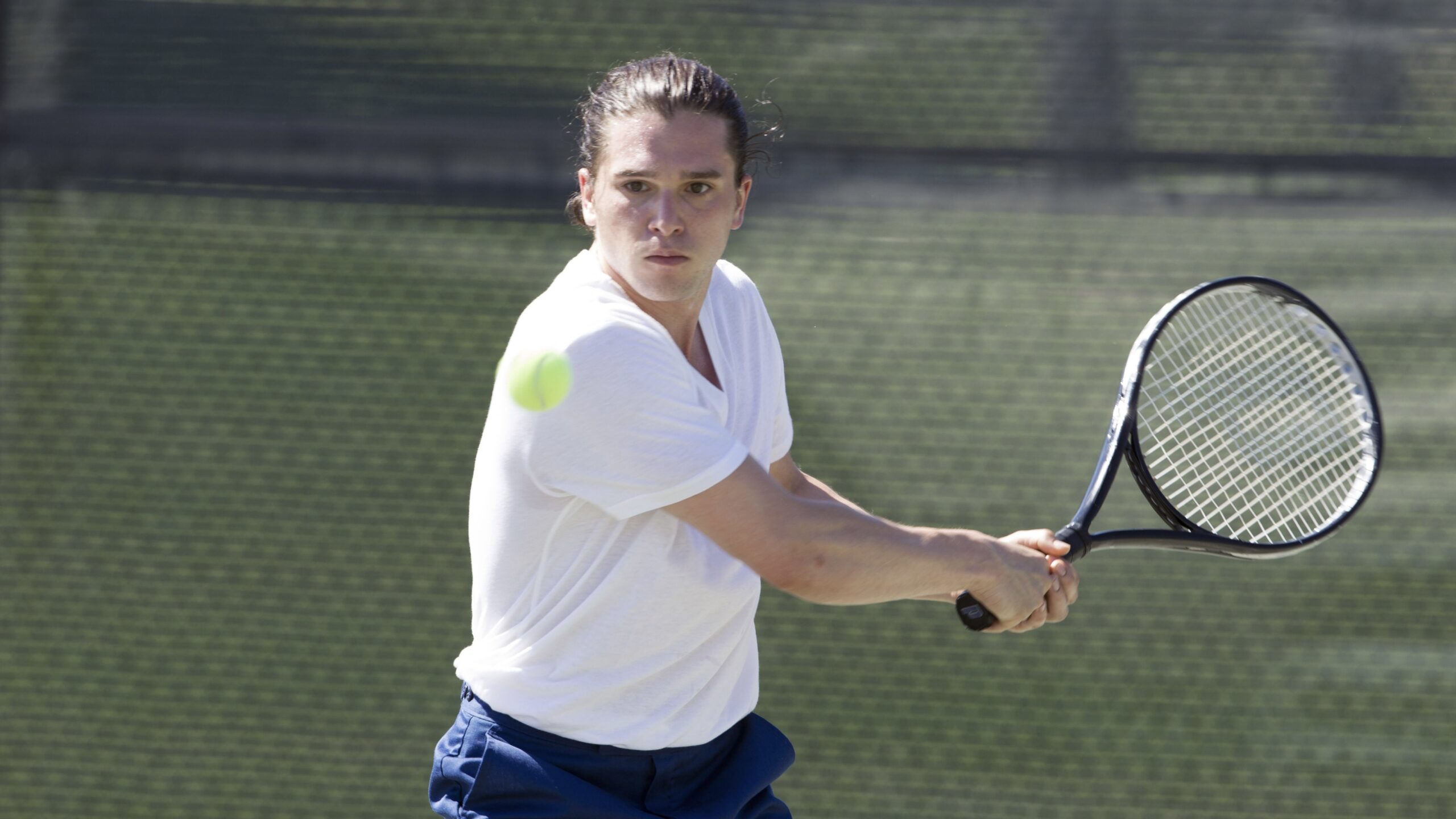 A tennis player in a white shirt hits a ball.