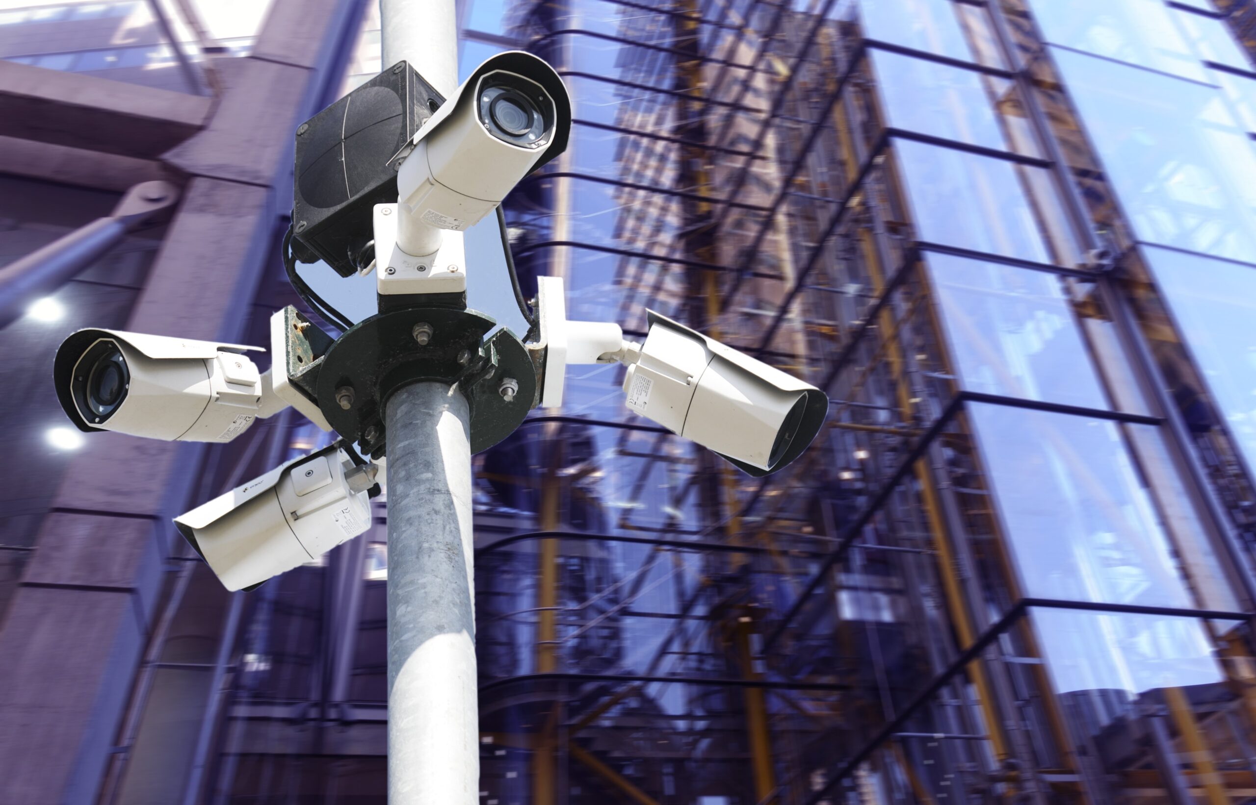 Several street surveillance cameras in front of a glass building.