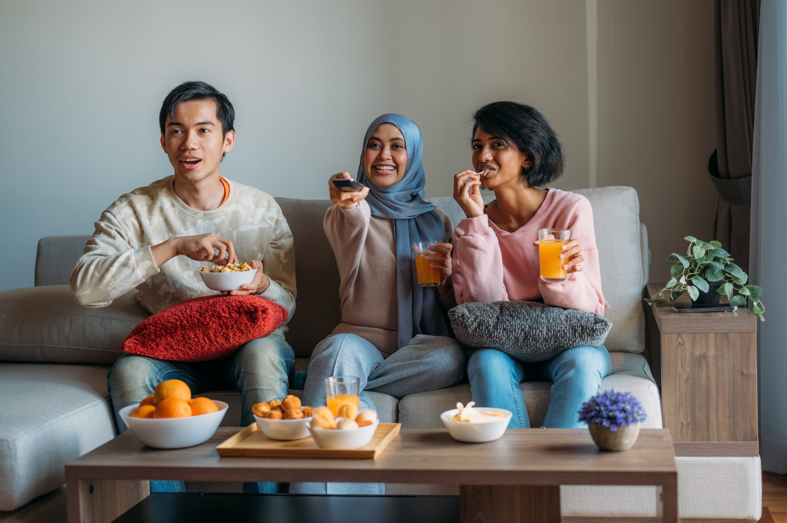 a group of three people sit together on a couch while drinking orange beverages from cups