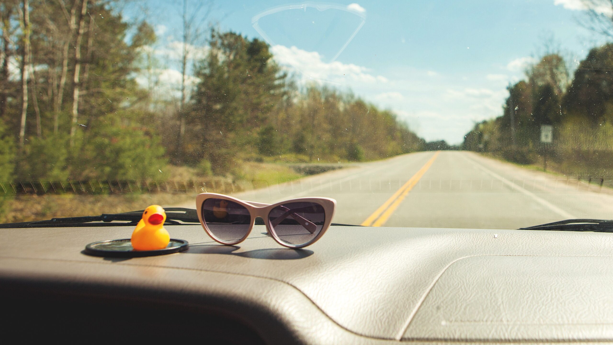 an old car dashboard with sunglasses and rubber ducky, sunny country scene in windshield