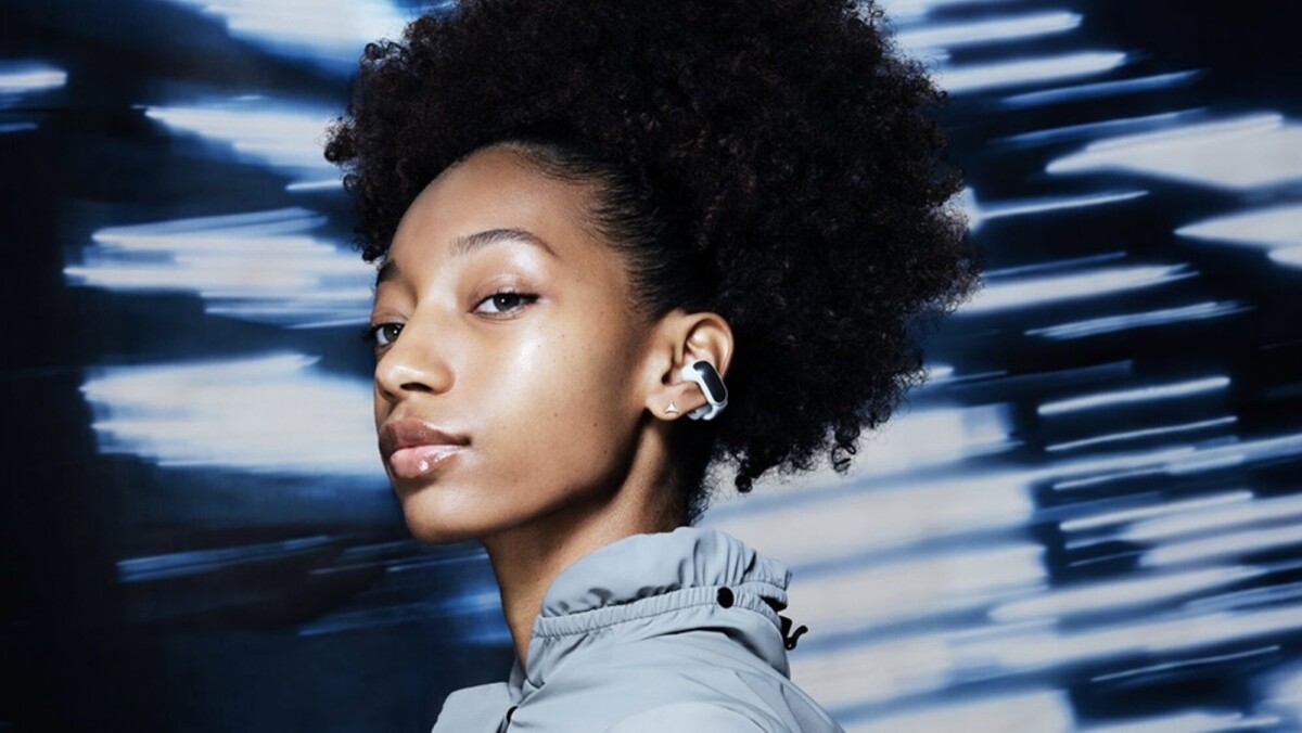 person on blue background wearing white and silver bose ultra open earbud