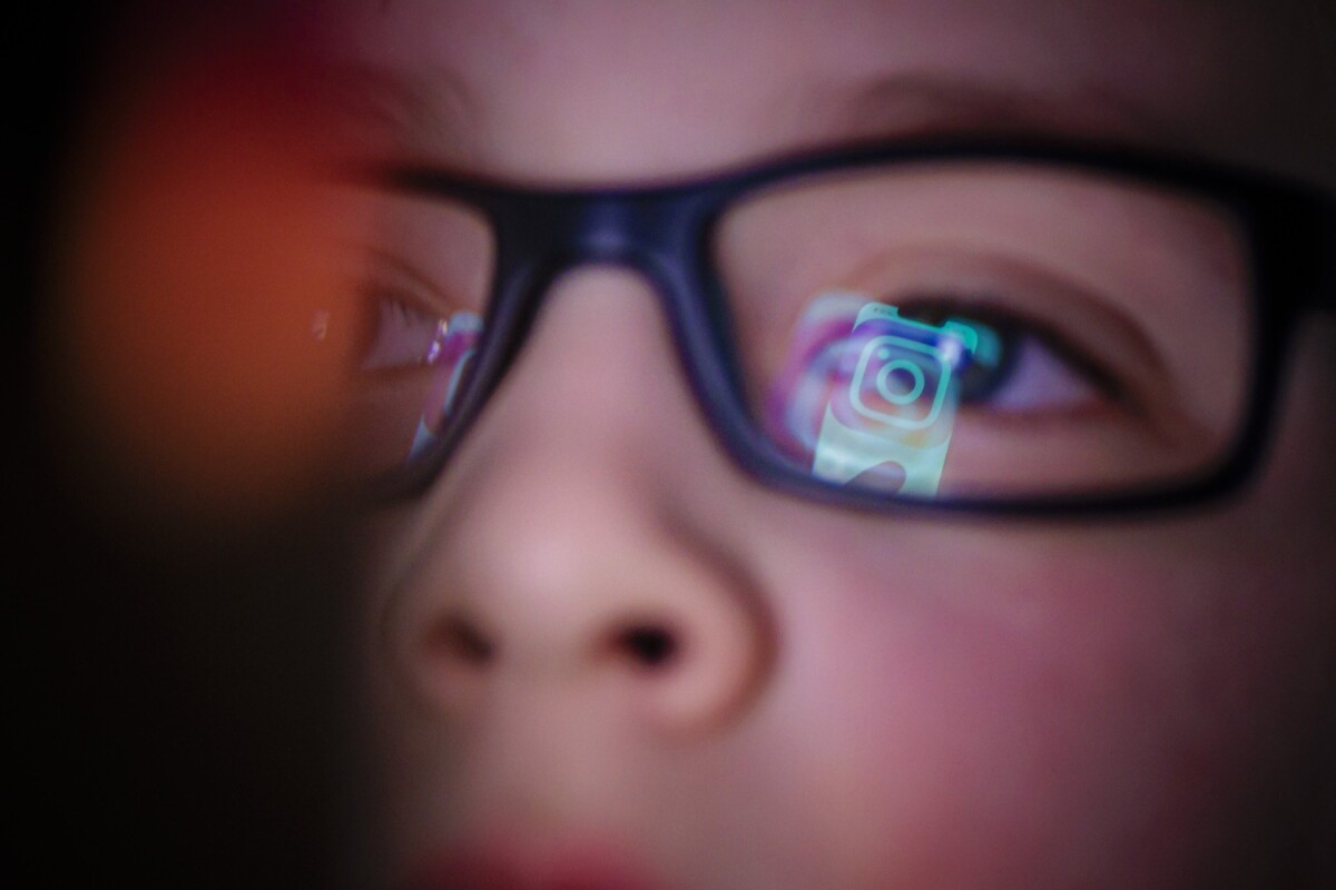 Instagram logo is reflected in boy's glasses.