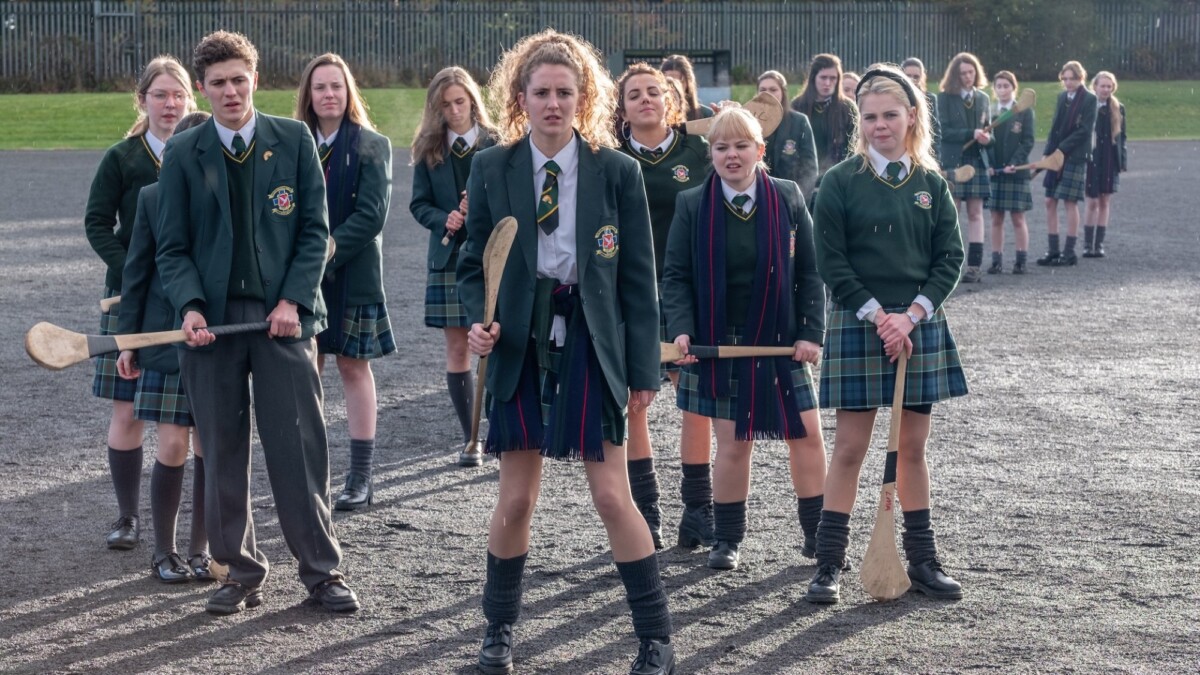 The cast of 'Derry Girls' in school uniforms playing lacrosse.